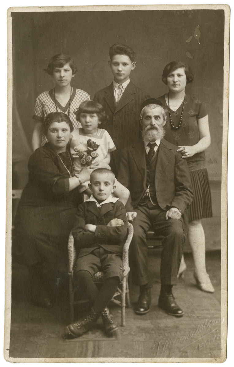Ita and Don Mordechai Adam pose for a portrait with their children. 

Standing (L to R) are the couple's elder children Fraidel, Sam, and Hinde. The couple's younger children Kaila (center) and  Moshe (seated) are also pictured.