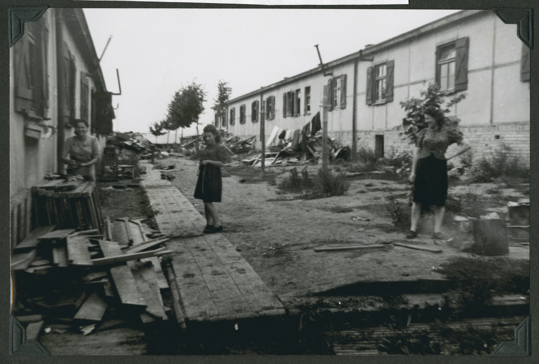 Women walk past debris strewn on a street in the Ziegenhain displaced persons camp.

The original caption reads: "Ziegenhain: Reconstruction.  The women wash their laundry amid the piles of debris the men were cleaning out."