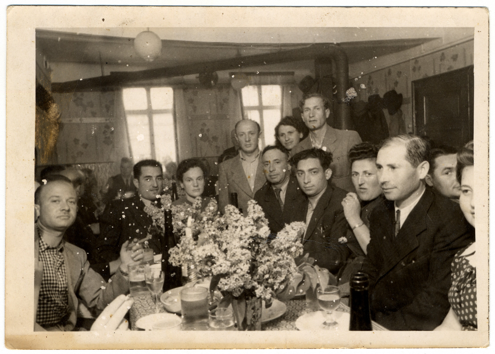 A group of displaced persons sits around a table in Zeilsheim following  a memorial service for victims of the Holocaust.

Roman Bol is pictured, standing in the back, on the right.  The man pictured second from the left has been identified as Leon Greenberg (later Green) of Gabin, Poland.