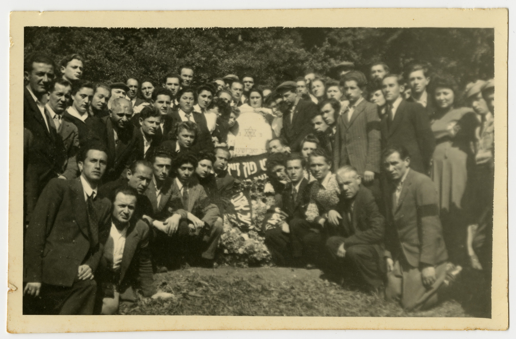 Displaced persons gather in remembrance of the Holocaust victims from Pruzhany, Poland. 

In the center is a memorial in the shape of a tombstone, banners and a wreath.