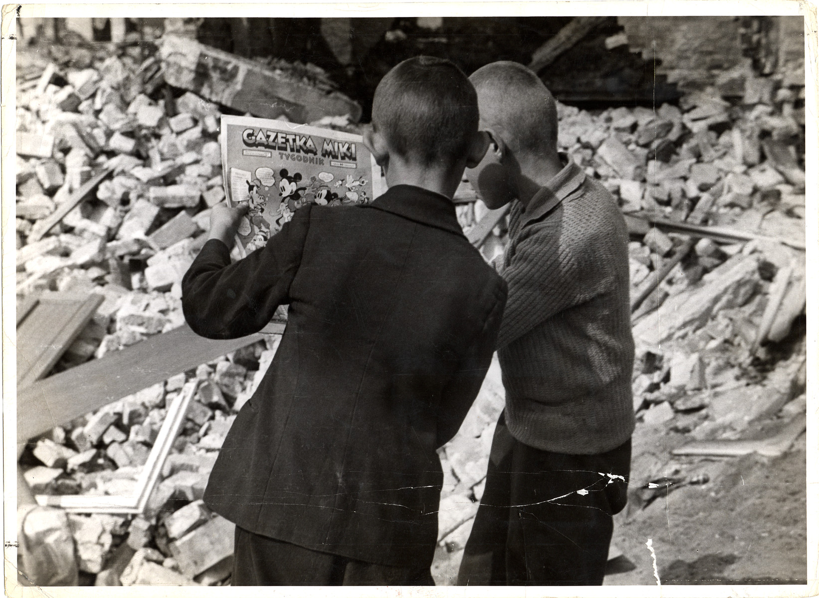 Two young Polish boys read a Polish edition of a Mickey Mouse Sunday colored supplement while standing among the ruins of a building in Warsaw.