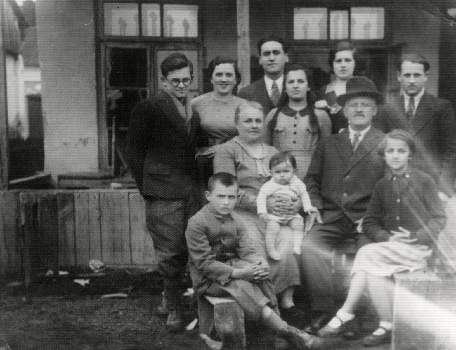 Prewar photograph Herskowicz family in front of their home.

Pictured are the grandparents Bezalel and Yehudit (nee Salomon) Herskowicz.  Yehudit is holding her grand daughter  Erica on her lap.  Seated on the far right is the youngest daughter Leah.  Standing in the center (with braids) is Tova.  Back row (left to right) are Zvi, Minna, Zvi Daniel and Rivka (nee Herskowicz) Daniel (the parents of Erica), and Ely Herskowicz.