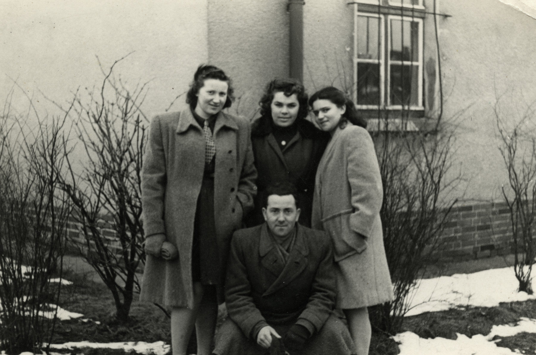 Friends pose in front of a building in the Bergen-Belsen displaced persons' camp. 

Pictured are Lili Deutsch (top left) wearing a coat made from a blanket, her sister Esther, and friend Leib (bottom).