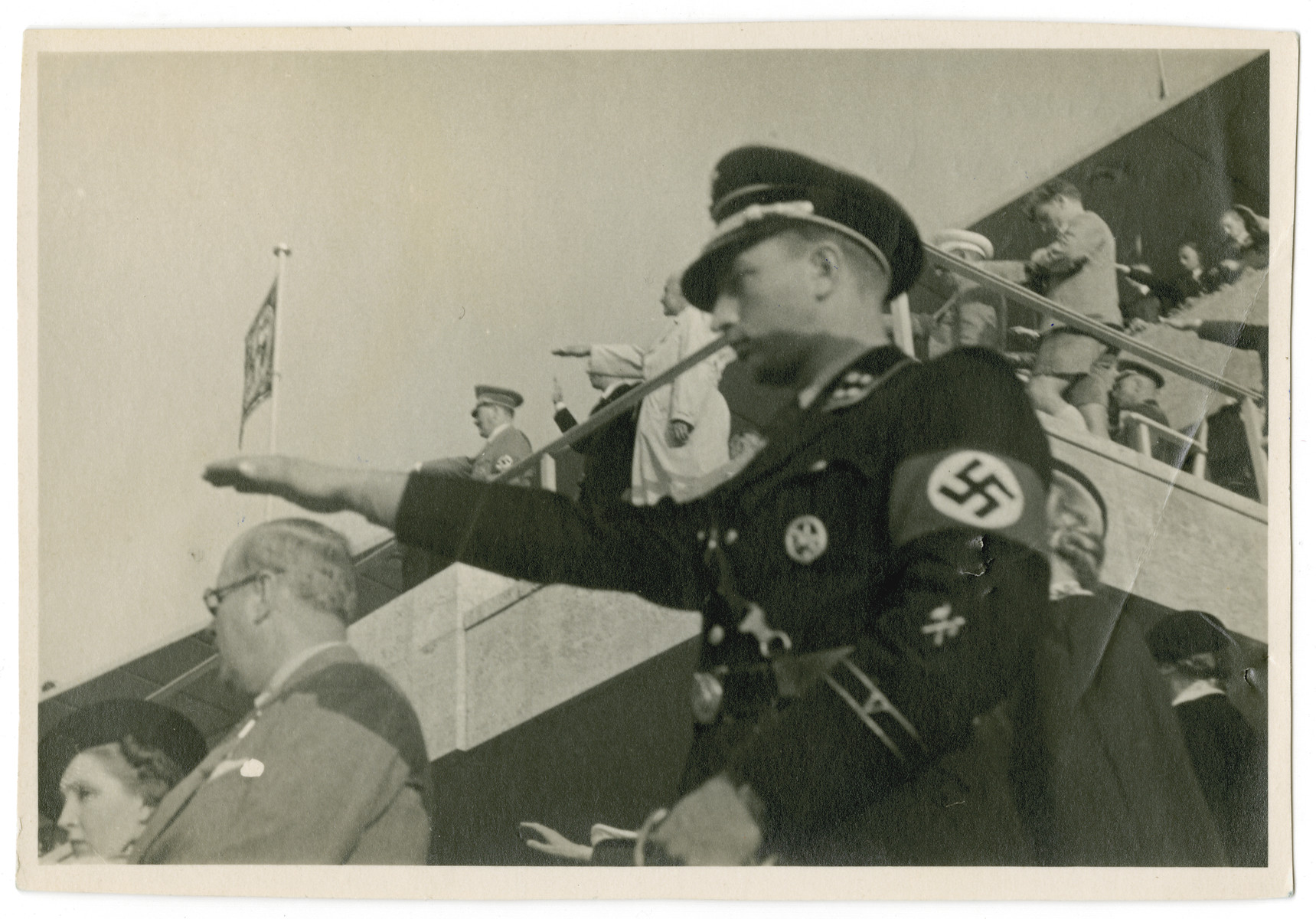 An SS man gives the Nazi salute at the start of the Berlin Olympics.

The saluting SS-man has been identified as SS-Sturmbannführer Hermnann Fegelein

The photograph was taken by Blanche Seimars (later Ensz) a young American woman visiting Germany from the United States.