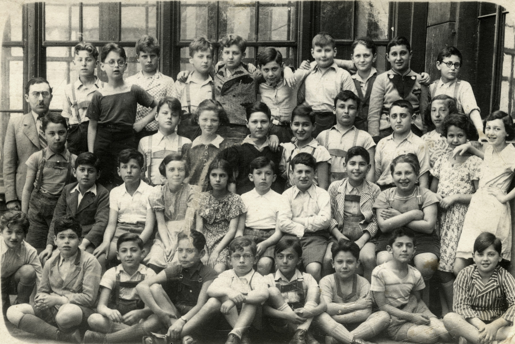 A group photograph of a class of the Chajes Realgymnasium in Vienna. 

Gerda Beruh (age 10)  is standing on the far right in a white dress.