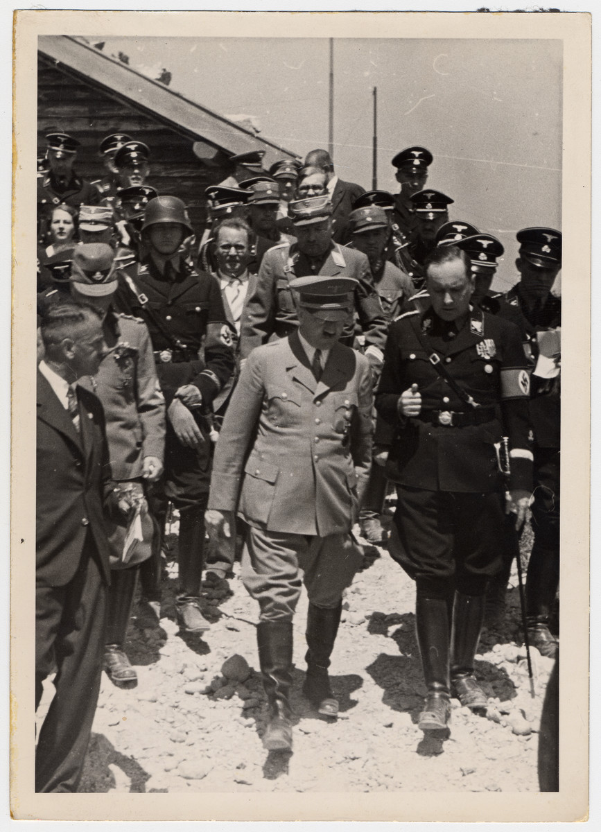 Adolph Hitler walks and converses with a Nazi official in the center of a large crowd of other Nazi soldiers.