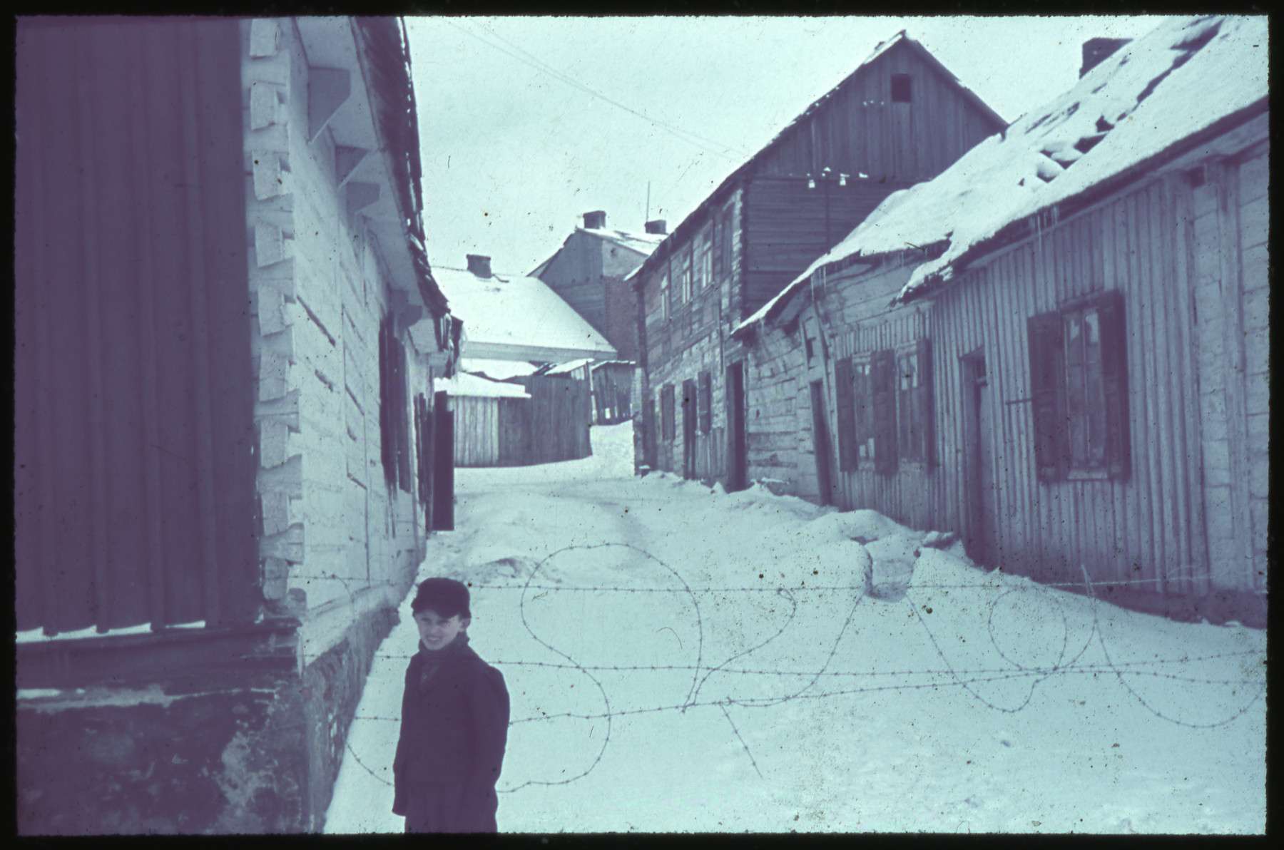 A young boy stands next to a barbed wire fence blocking off a snow-covered road in Kozienice.