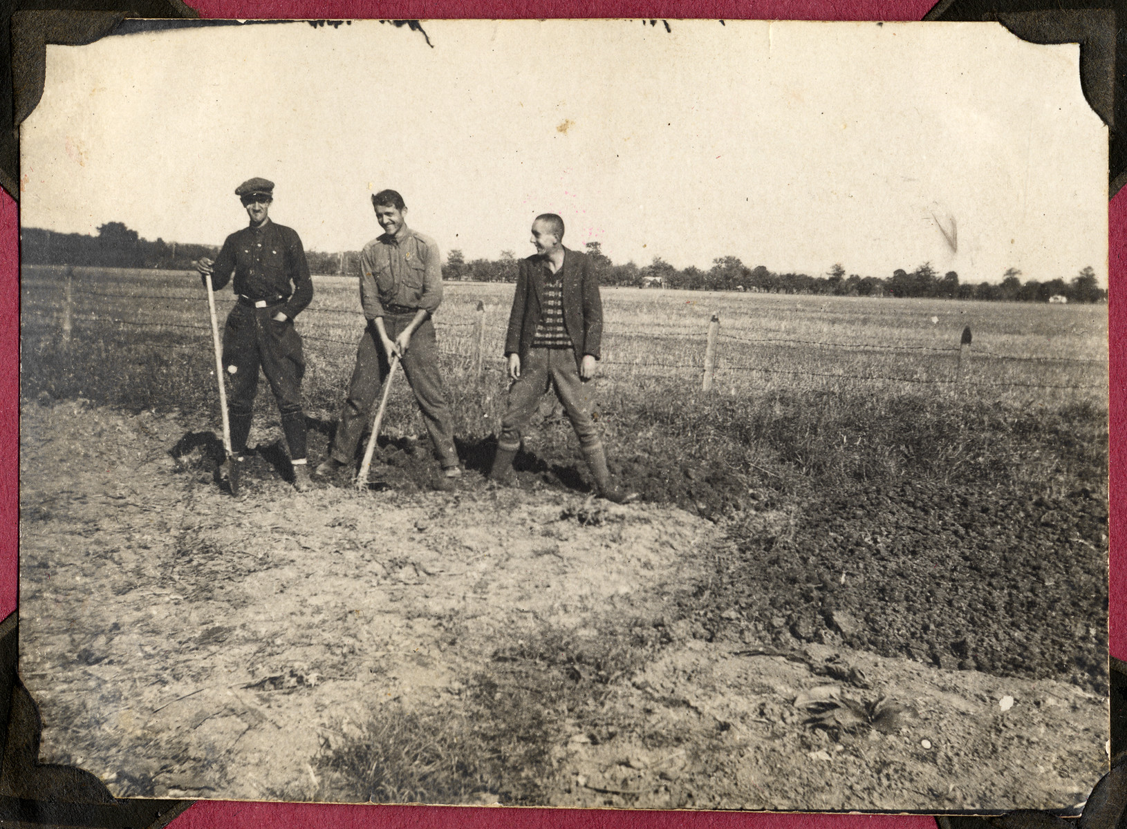 Three unidentified young men pose with farm tools in an unidentified field.