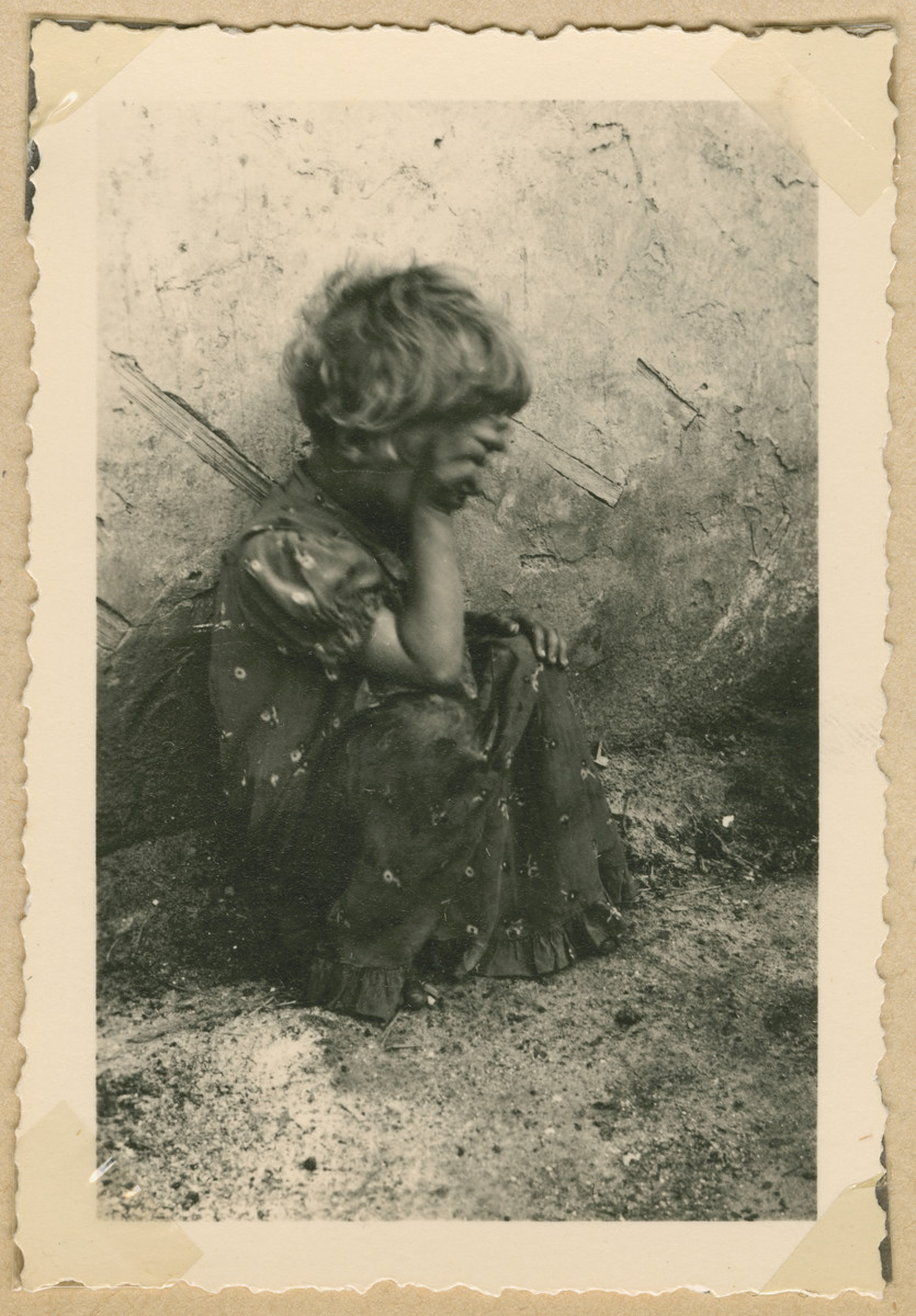 A young Jewish girl with her hand obscuring her face sits outside in Deblin-Irena.