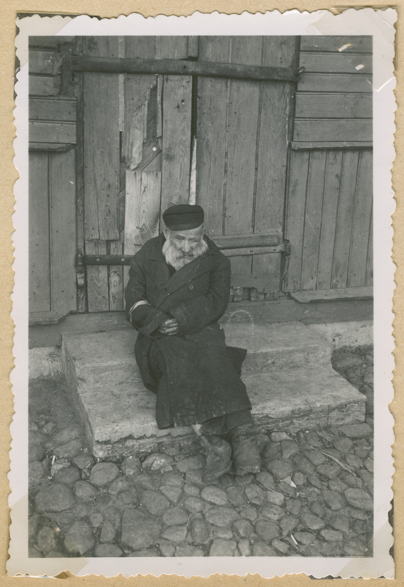 An elderly Jewish man wearing an armband sits on the stoop of a building in Deblin-Irena.