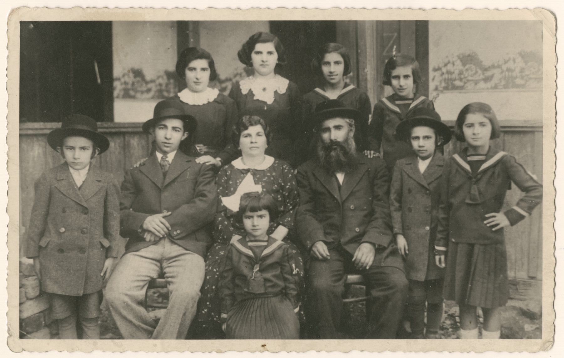 Group portrait of a large religious family, the Smilovic family, in Munkachevo.

Pictured left to right (front row): Sziku, Isaac Leib, Chana, Eva in front of her, Mordche Shmiel, Berl, Freidl.  (back row): Sheindel, Golde, Heddy and Rivke.

Chana, Mordechai Shmuel, Golda and her four year old son, and Eva perished in Auschwitz in May 1944.  Beryl was liberated from Mauthausen but never heard from again.