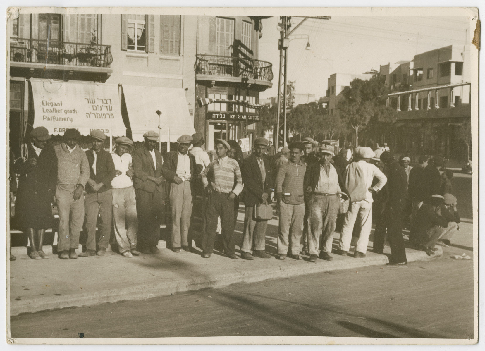 Unemployed workers queue up on a street in Israel.

Photograph is used on page 267 of Robert Gessner's "Some of My Best Friends are Jews."The typed caption attached to the photograph reads, "Unemployed Jewish workers waiting on the open market for an employer."