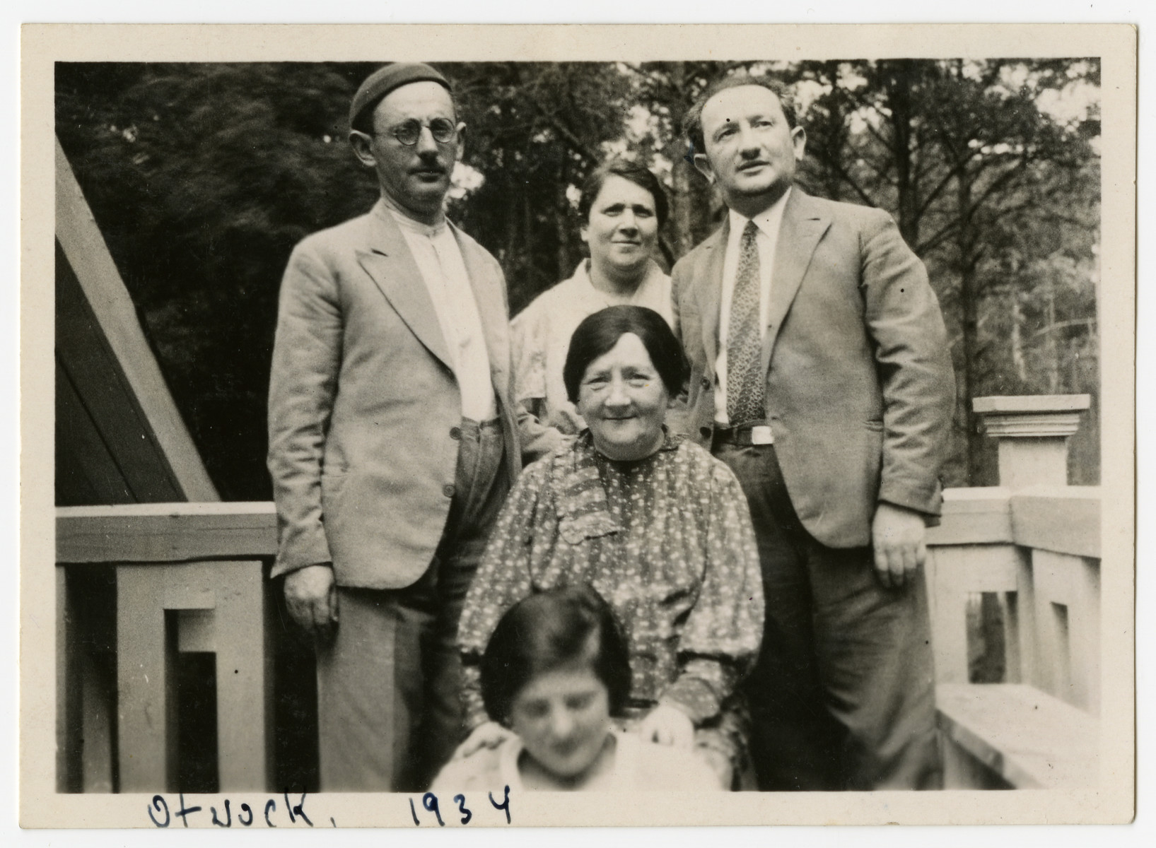 Miriam Rabinowitz sits on a porch surrounded by her children and granddaughter. 

In the front is Celinka Rabinowitz (Szyja's daughter).  Standing from left to right are Szyja, Doba (Szyja's wife) and Pinchas Rabinowitz.