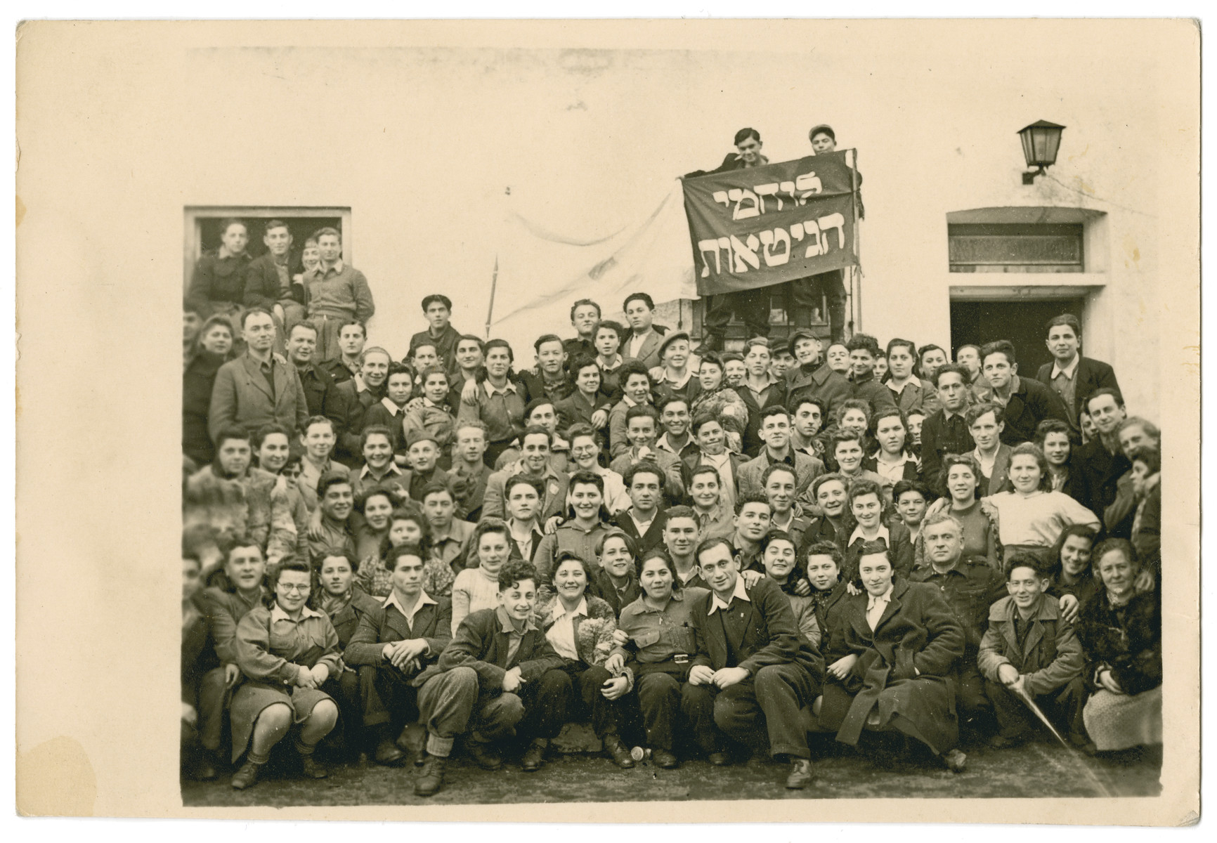 A large group of Jewish displaced persons poses in front of a banner that says "Ghetto Fighters."