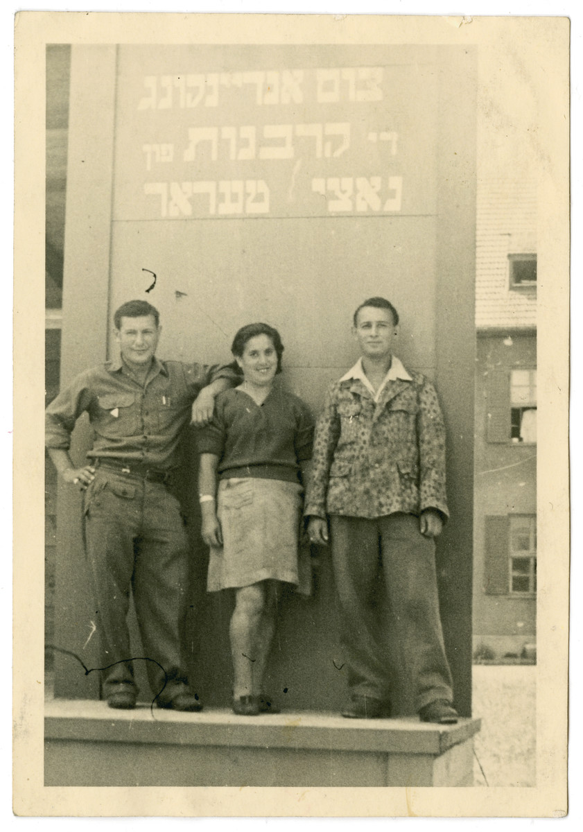 Three Jewish displaced persons pose in front of a memorial to the victims of the Holocaust.

The Yiddish memorial reads: "As a memory to those sacrificed to Nazi terror."