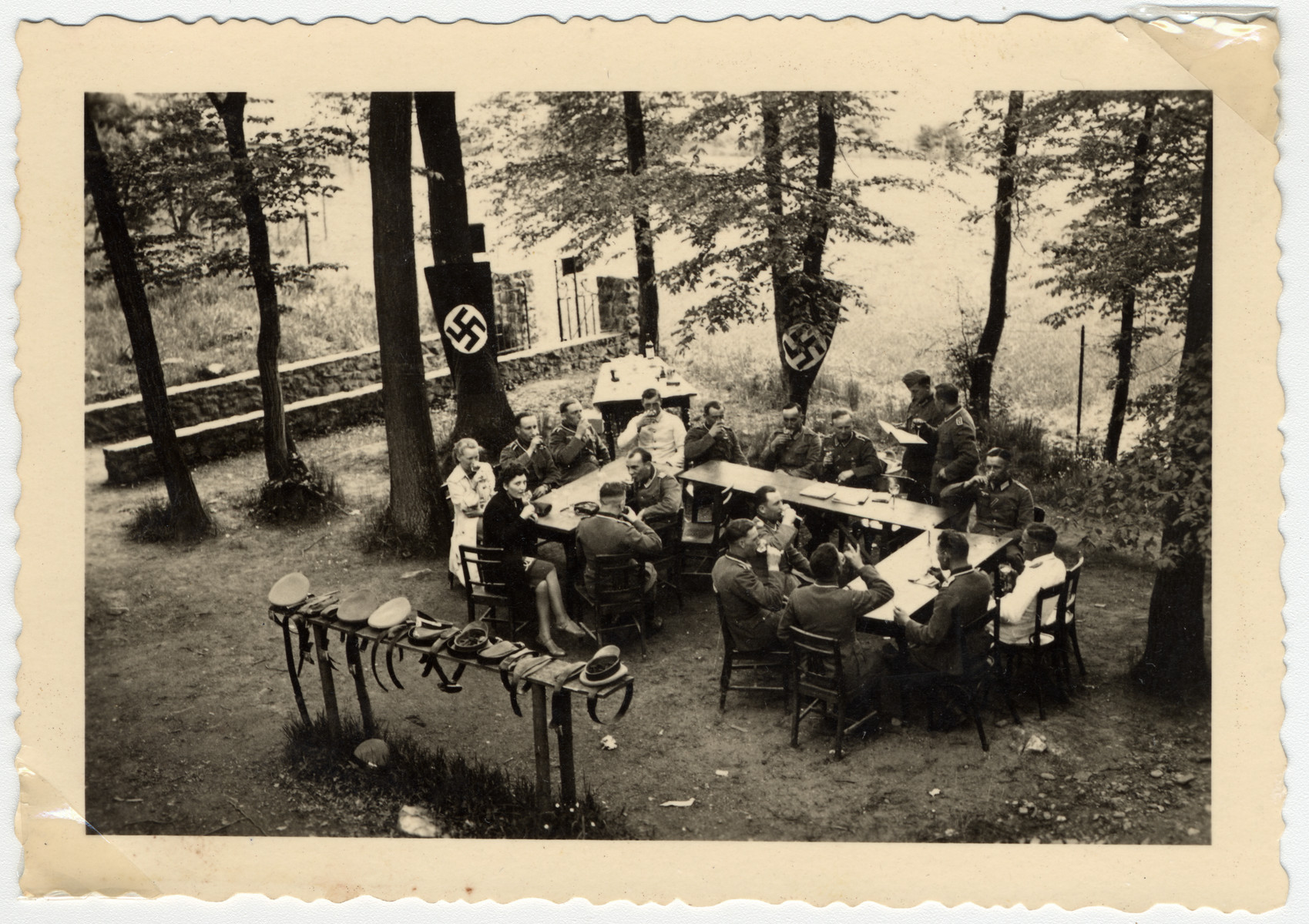 Unidentified people sit eating and drinking with a Nazi flag in the background.