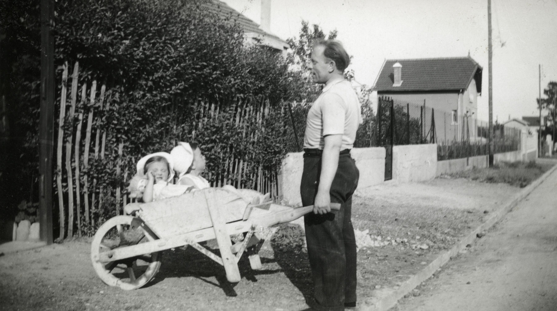 A Jewish father pushes his two young children in a wheelbarrow, near their home in Gagny, a suburb of Paris.

Pictured are Hersh Jakubovitch and his children Fernande and Albert.