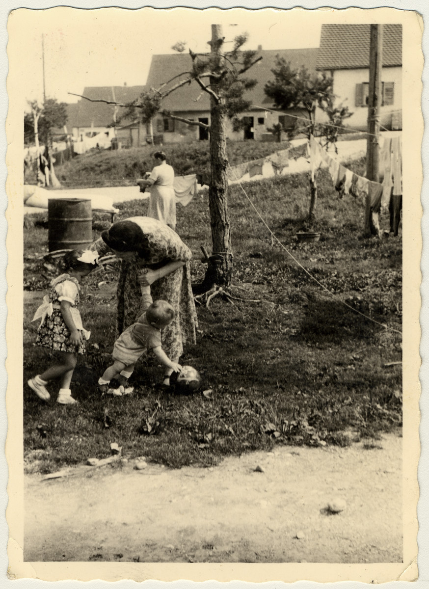 A woman attends to two children while laundry hangs in the background, probably in the Foehrenwald displaced persons camp.