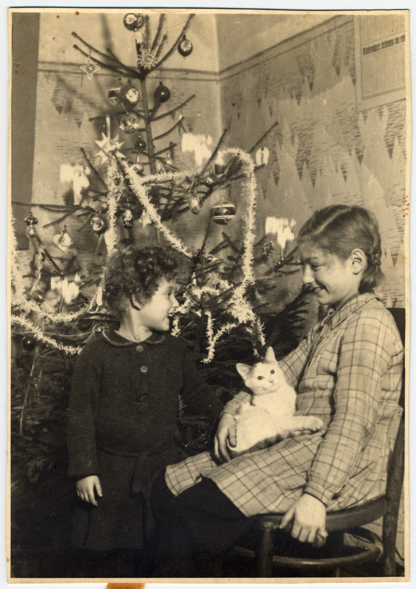 Halina and Eva Litman stand pose next to a Christmas tree while in hiding in Tluste in a washer woman's house.