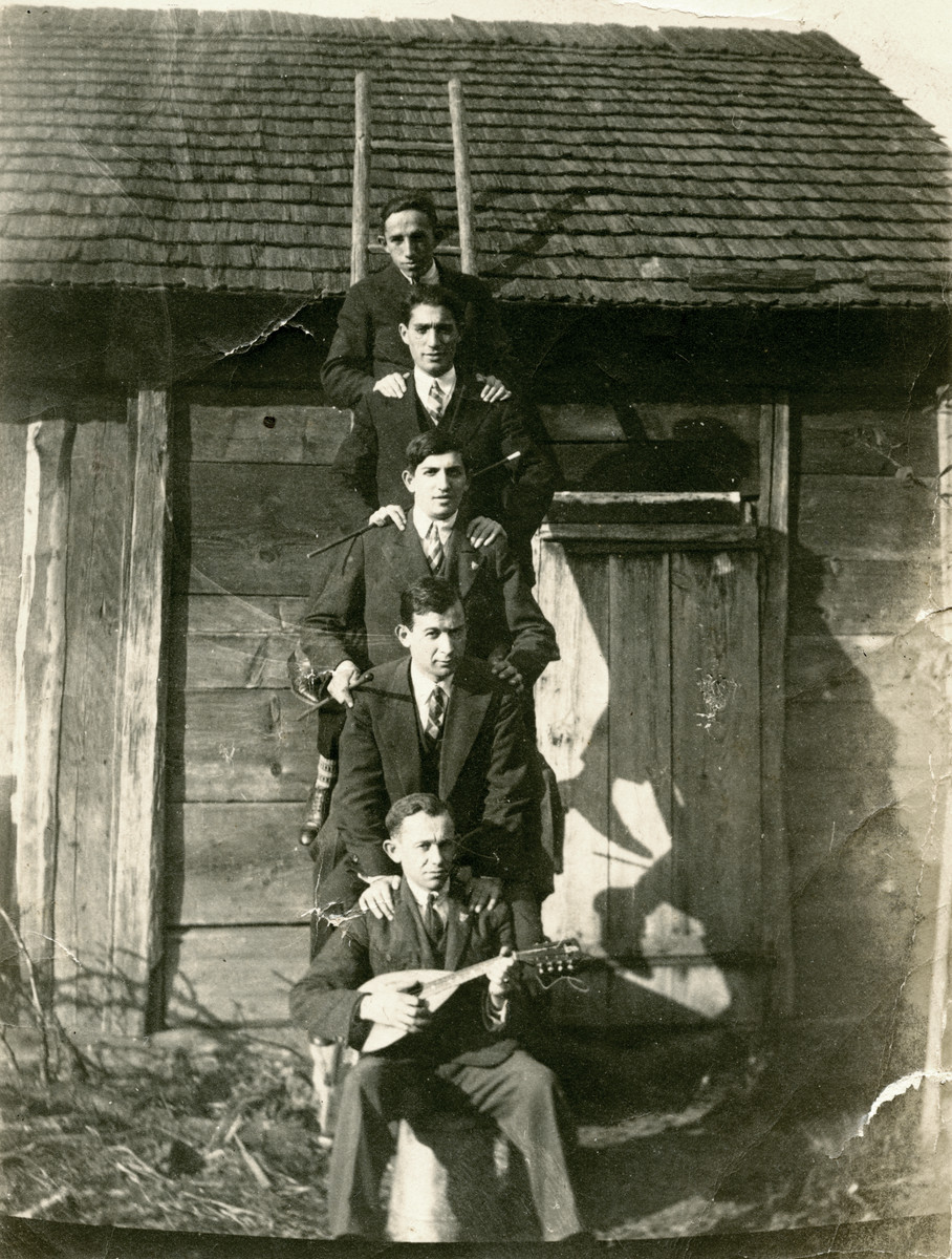 Five young male students posie on the rungs of a ladder outside of a building that looks like a barn or shed. 

Feivel Frankfowicz is pictured on the bottom of the ladder holding a mandolin