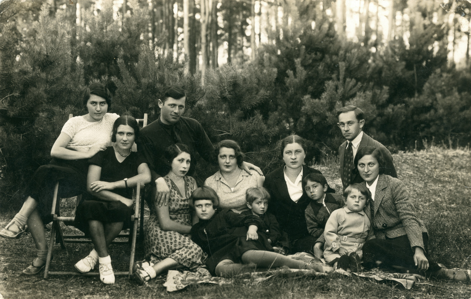 A group of men. women and children sit outside by a wooded area. 

Two women are sitting in a chair and the others are sitting on a blanket. Feivel Frankfowicz is pictured in the back row on the far right. His sister in law, Sara Frankow, is seated in front of him.