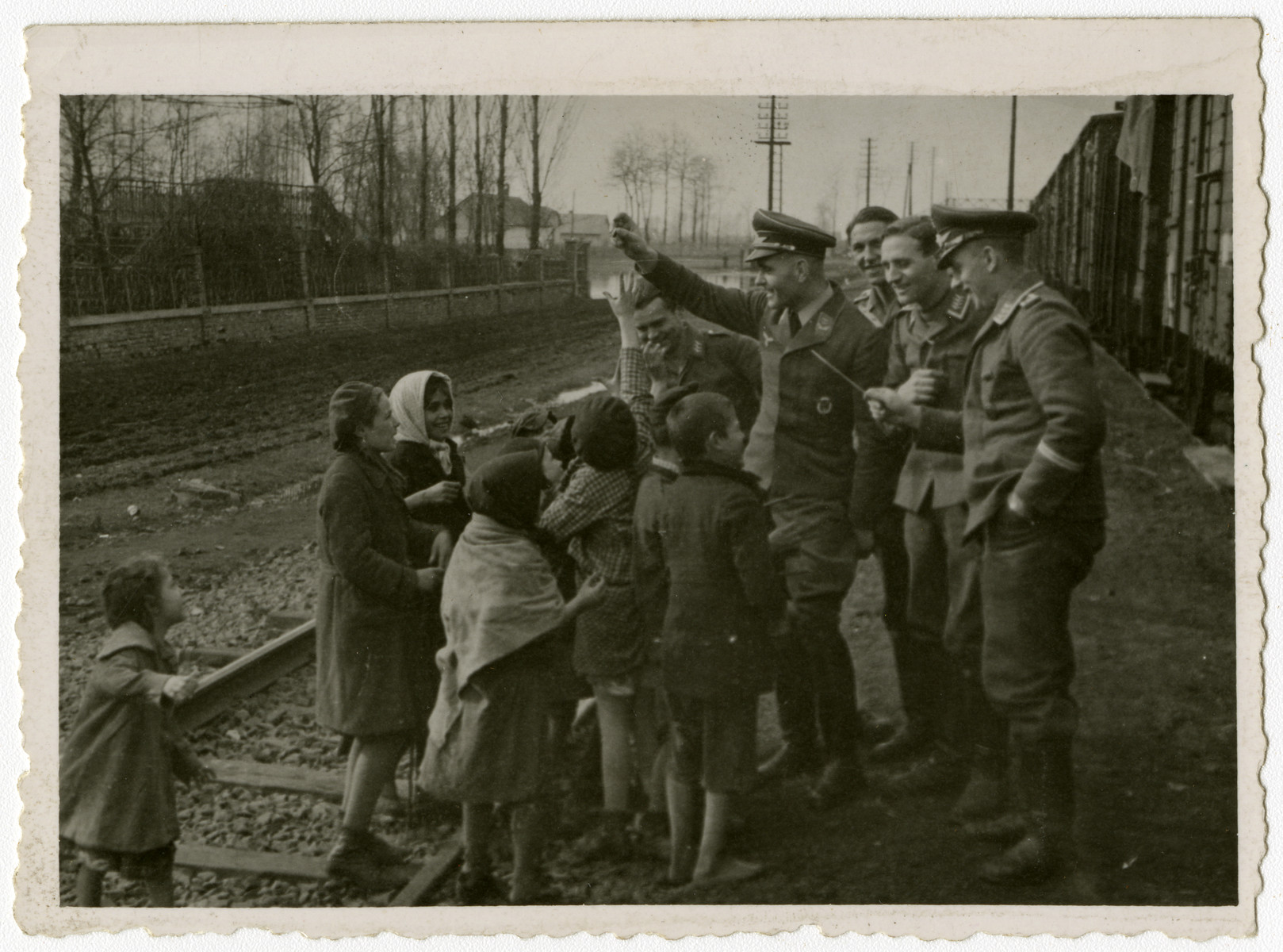 Members of the German Luftwaffe engage with local children by the tracks of an unidentified railway.

This image is one contained in an album found by Jacob Igra in an apartment in Sosnowiec after the war. Many of the photographs are believed to have been taken by a soldier with the SD-SIPO (Sicherheitspolizei) following the invasion of Poland in 1939. Additional photographs depict einsatzgruppen activities at sites throughout Nazi occupied Eastern Europe and may have been later additions to the album.
