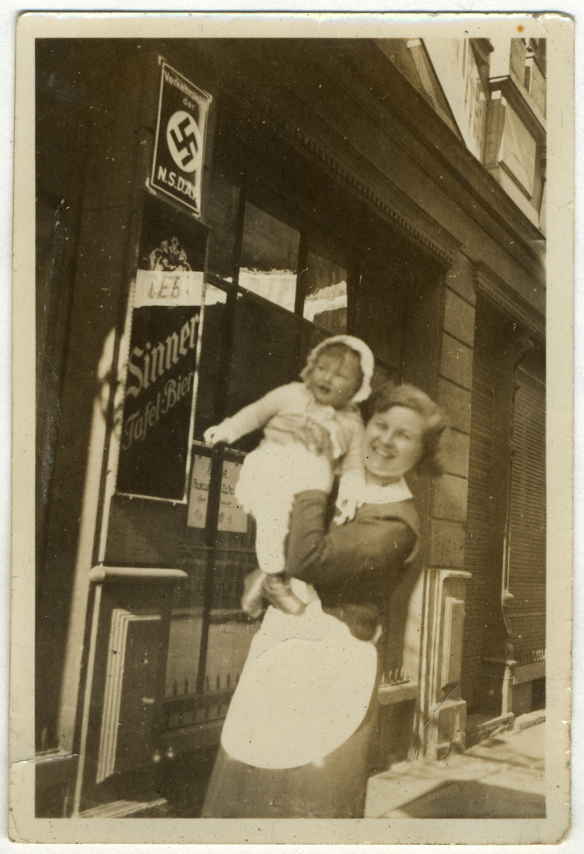 A German nanny holds Ellen Kaelbermann outside a business in Mannheim, Germany adorned with a Nazi poster.