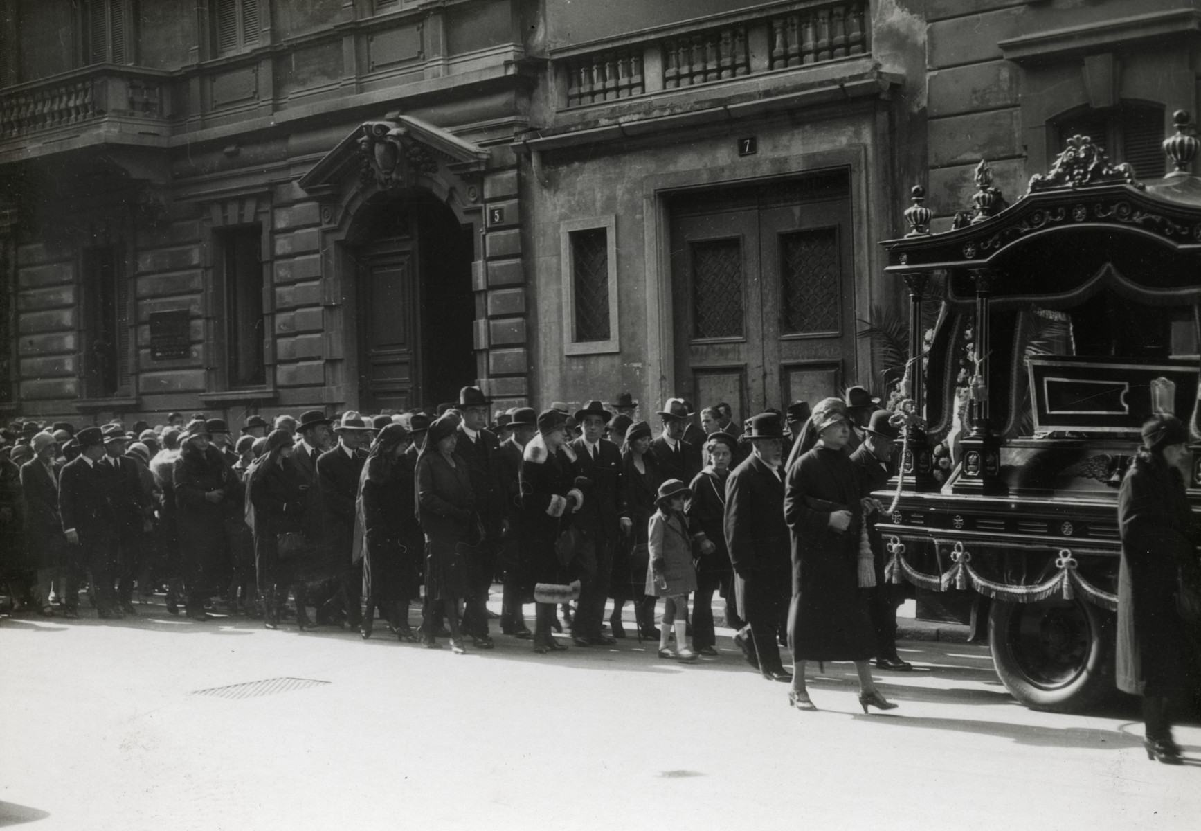 A procession walks down a street of Milan during the funeral of Eliza Navarra (Dario's grandmother).
