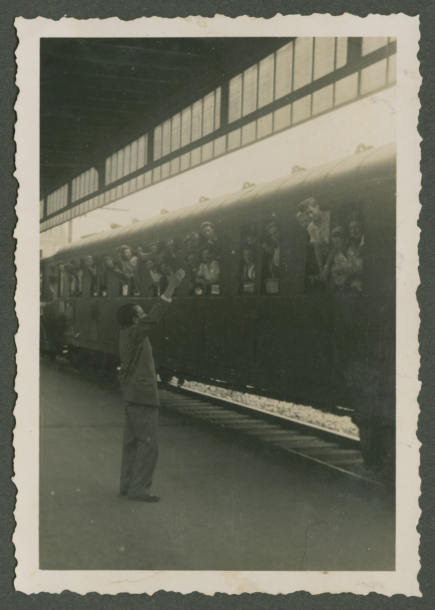 Children lean out the windows of a train and wave goodbye [probably as they prepare to depart for Palestine.]