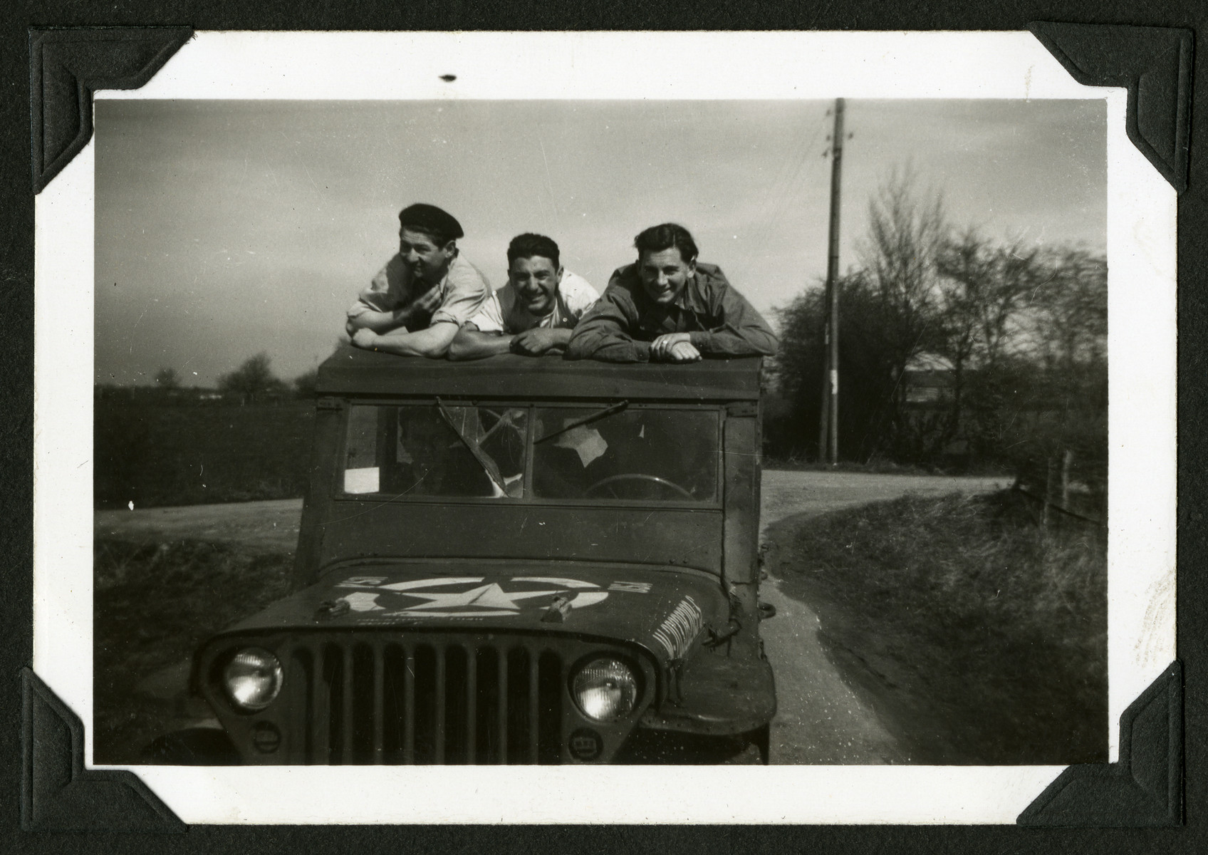 Three members of a hachshara in Leve, Belgium lean against the roof of a jeep.