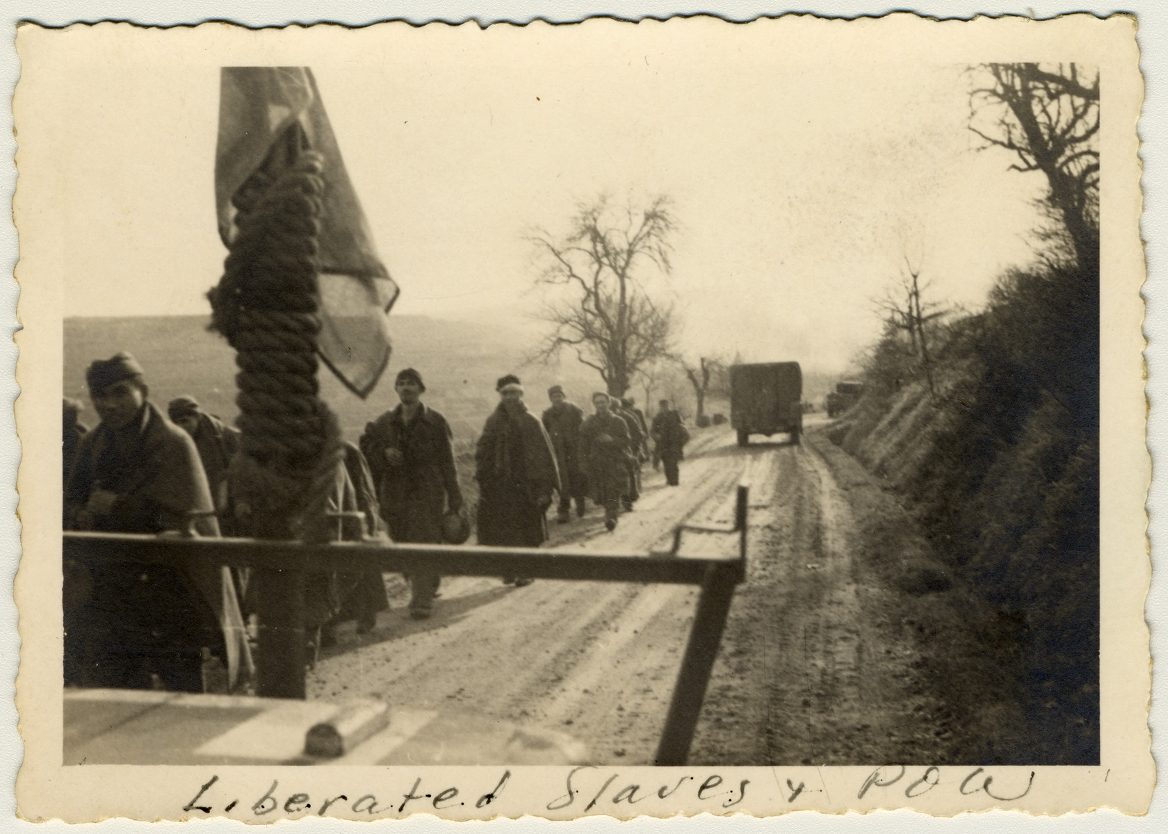 Camp survivors and freed POWs march down a road after their liberation.

The original caption reads: "Liberated slaves and POW."