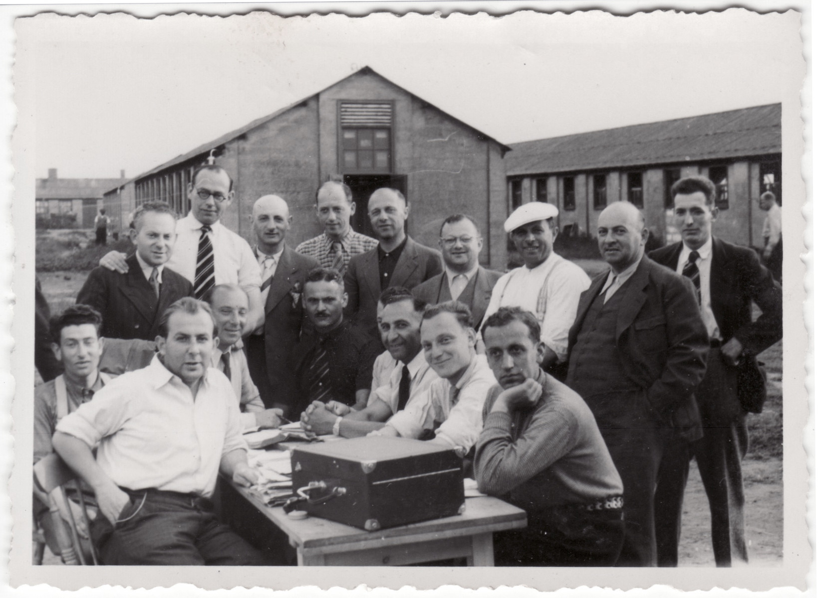 Jewish refugees gather around a record player on top of an outdoor table at the Kitchener refugee camp.

Siegfried Kulmann is pictured in the lower left in a white short sleeve shirt.