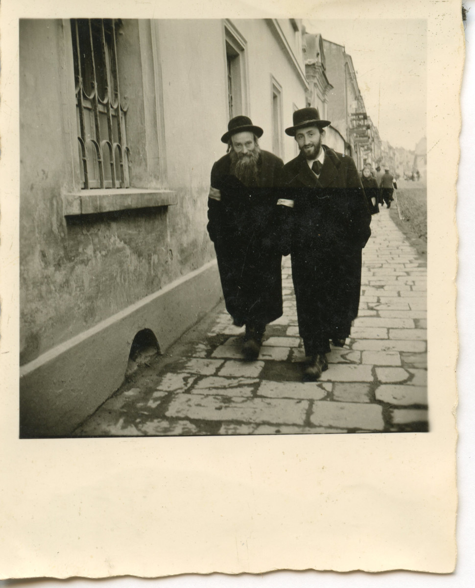 Two religious Jewish men walk down a ghetto street [perhaps in Osieciny].