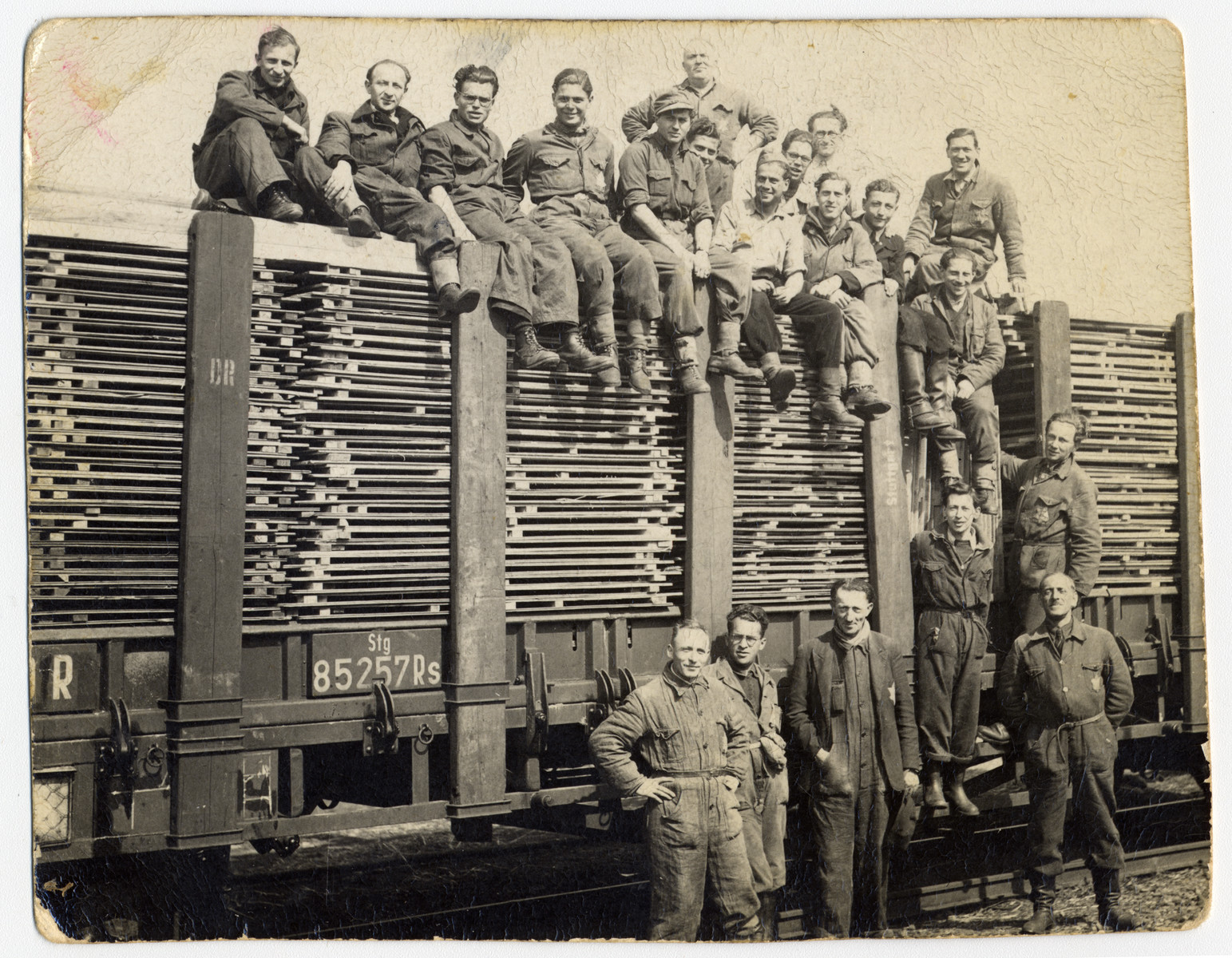 Jewish internees pose on top and next to a railcar loaded with planks of lumber in Westerbork. 

Ignatz Kempler is standing at the base of train (second from right).