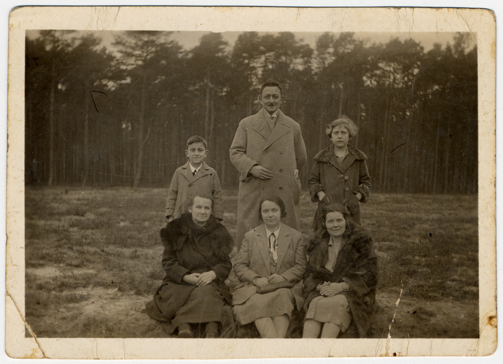 Standing from left to right are Hans, Max, and Ilse Hanauer.  Below them (from left to right) sit Marie Teske, Frieda Hanauer, and an unknown woman.  The family is posing in front of a forest.