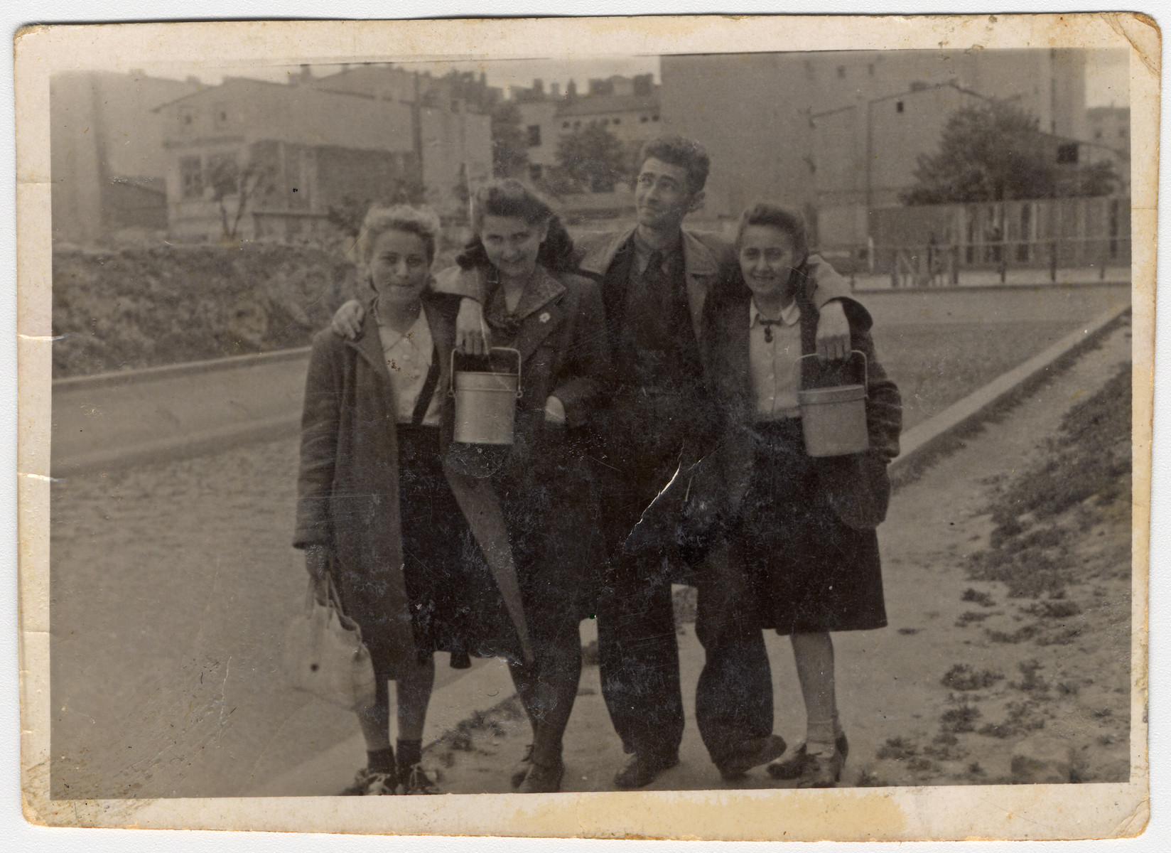 A group of teenagers hold lunch pails in case there will be a distribution of soup while standing in on Marynarska street in the Lodz ghetto.  

Pictured from the left are: Rozka Grosman (later Zilbar -- Mendel Grosman's sister), Rachel Beim, Arie Princ (later Ben Menachem) and his fiancee Ewa Bialer.