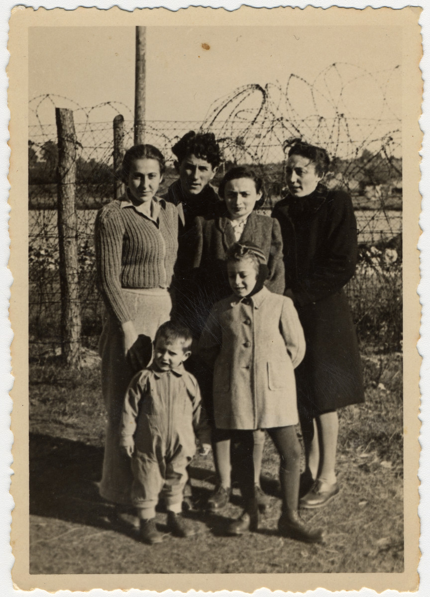 Jewish DPs pose together in front of a barbed wire fence. 
 
Pictured on the left are Giza and Reuwen Wiernik and their son Alexander.