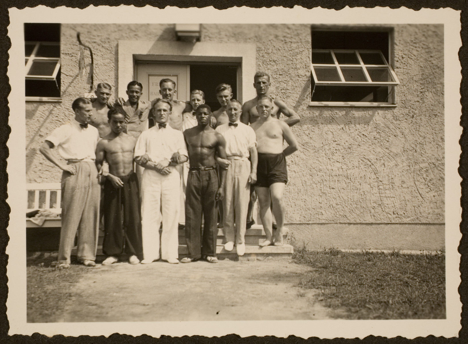 A group of athletes pose in front of one of the residences in the Olympic village.  Among those pictured is American athlete, Archie Williams, fourth  from the left. 

The identities of the other athletes is unknown.