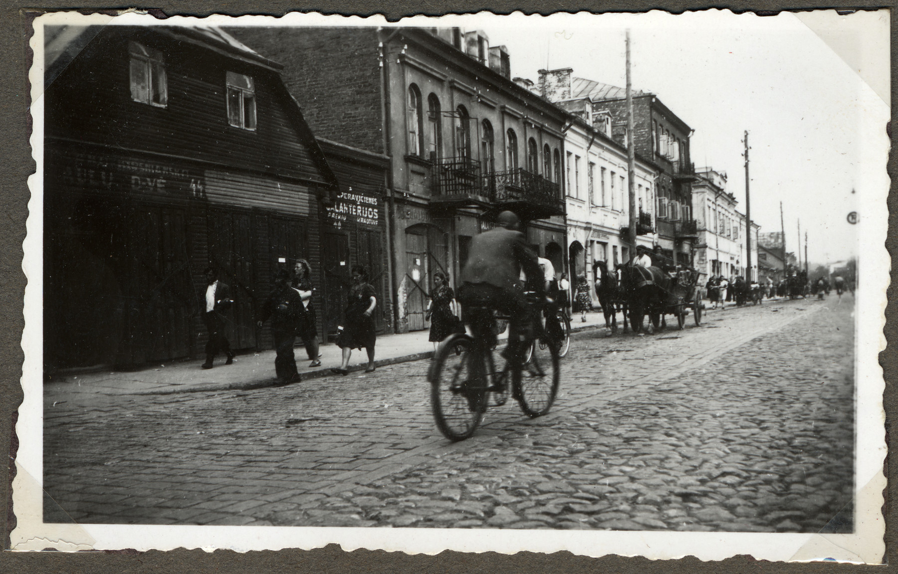 A Lithuanian man rides his bicycle down a street in Kaunas while in the other direction Jews move their belongings on carts and wagons to the new ghetto located across the river in Slobodka.