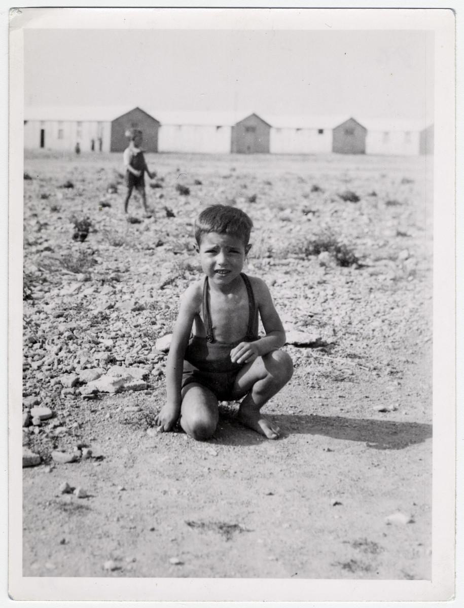 A small boy [probably Spanish] crouches down, as he plays in the dirt in front of the barracks of the Rivesaltes internment camp. 

Original caption reads: "Pepito."