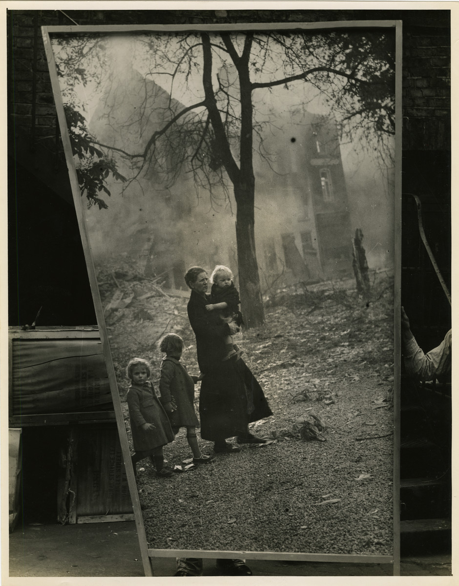 Panel from a 1944 exhibition in London, England entitled "Germany- the Evidence" showing a woman and young children near a destroyed building. 

The back of the photo reads "British Official Photograph; Distrbuted by the Ministry of Information. D. ; The Evil We Fight.; Ministry of Information Exhibition priduced by Display & Exhibitions Division for show all over Great Britain.; Display panel"