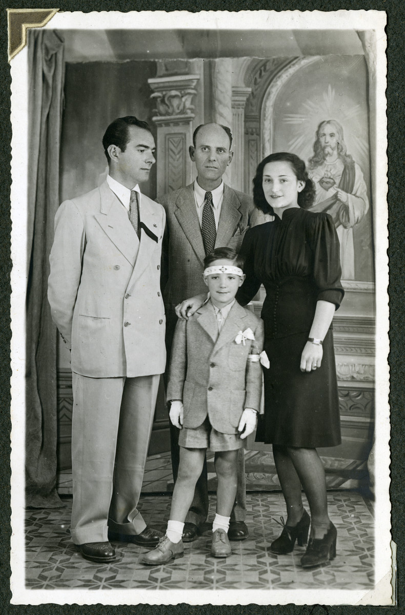 Romano Pelligrino poses with his parents, Helga and Mario and an unidentified man in front of a painting of Jesus.  Romano is wearing a white armband and his father is wearing a black mourning badge.