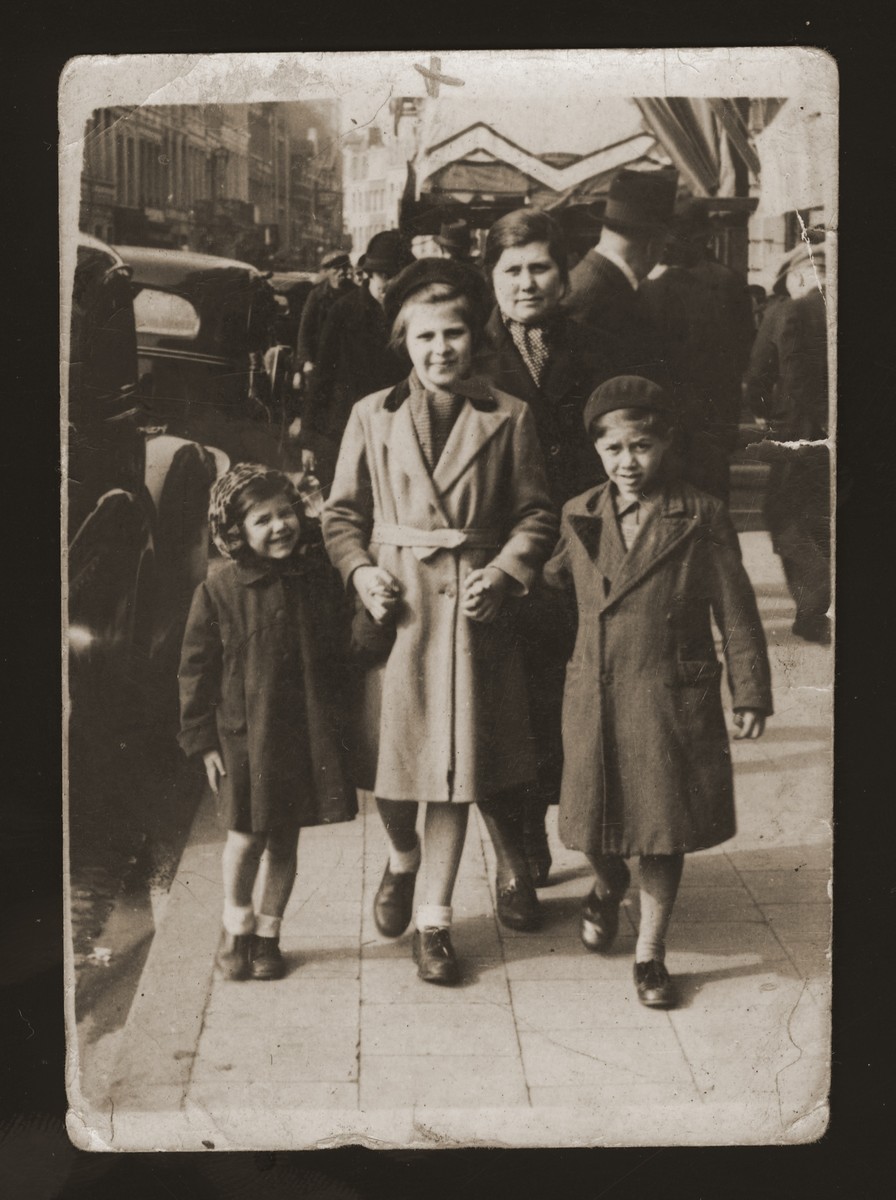 The Zalc children walk with their older cousin along a major street in Antwerp.  

Pictured from left to right are: Lucie Zalc, Sara Kierschner, and Andre Zalc.  Mirjana Zalc walks behind the three children.  Sara was the daughter of Gusta Ullman and David Kierschner, the sister and brother-in-law of Mirjana Zalc.
