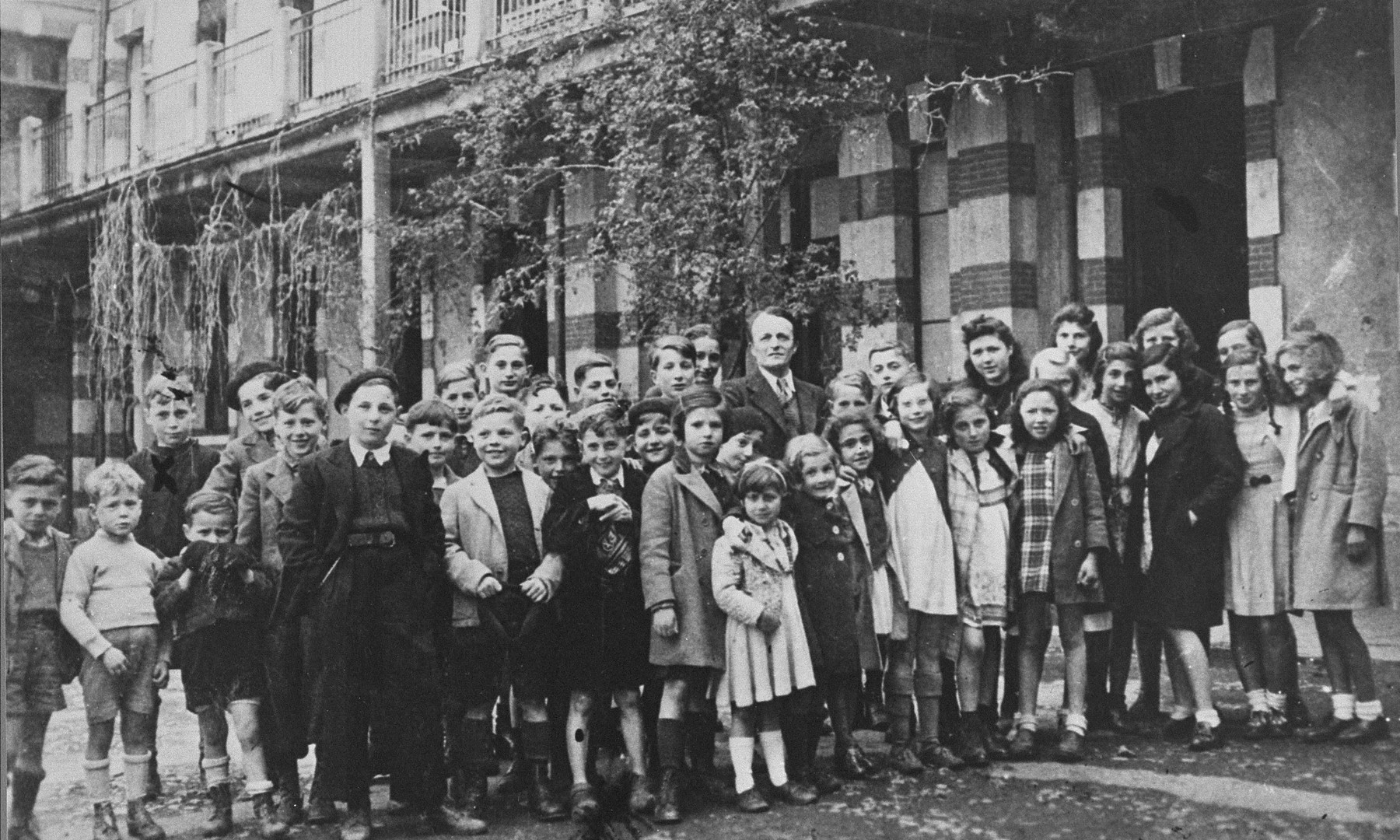 Group portrait of Jewish children at the OSE home, "Maison des Pupilles de la Nation," in Aspet, France.  

Standing in the middle of the group is the director, Henri Couvot.  Michael Oppenheimer is pictured in the last row, second from the left, his face partially hidden.  

The children were brought to the home from French transit camps with the assistance of the American Friends Service Committee (AFSC) and the Oeuvre de secours aux enfants (OSE).