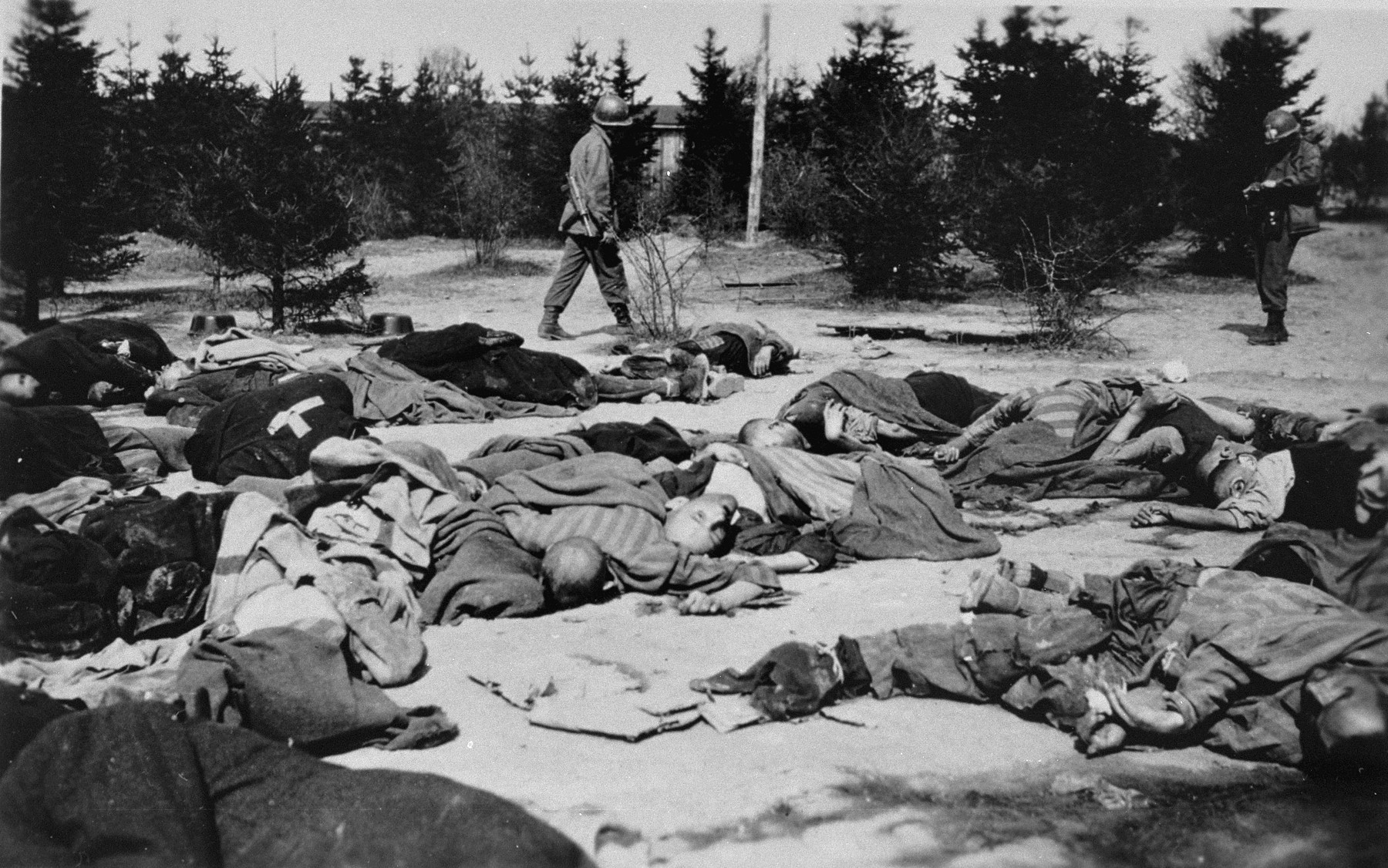 American soldiers view the bodies of prisoners that lie strewn on the ground in the newly liberated Ohrdruf concentration camp.