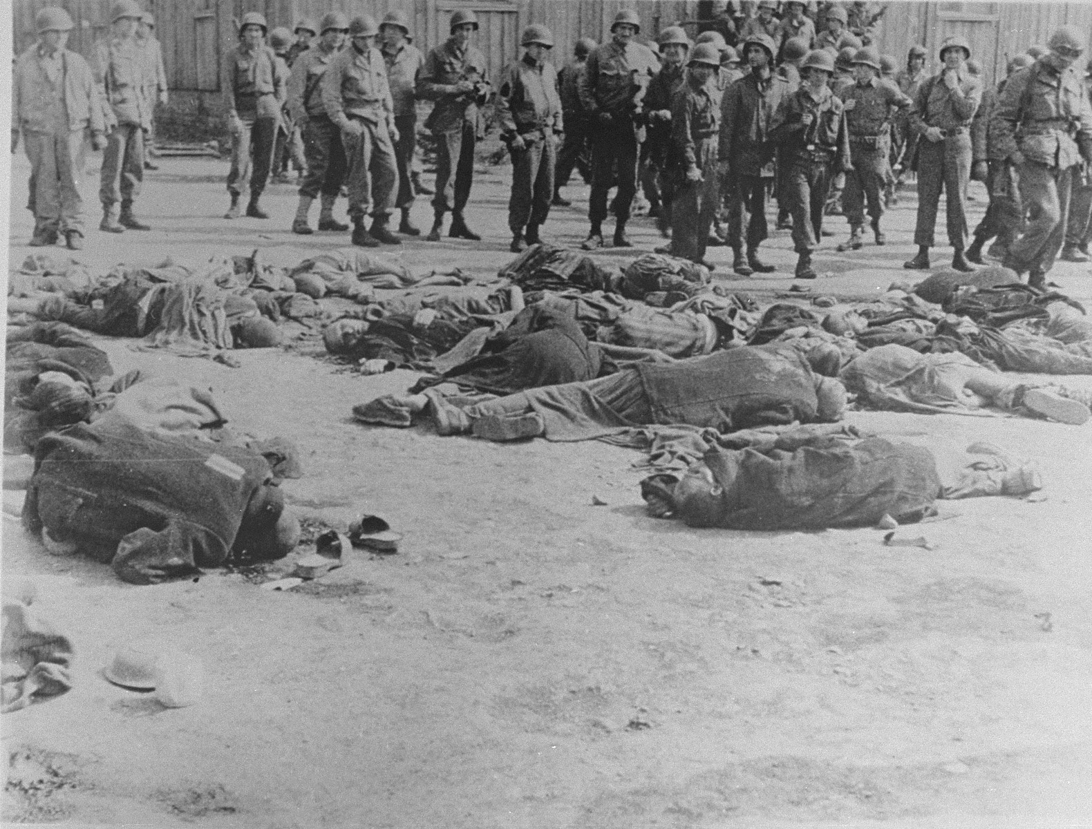American soldiers view the bodies of prisoners that lie strewn on the ground in the newly liberated Ohrdruf concentration camp.