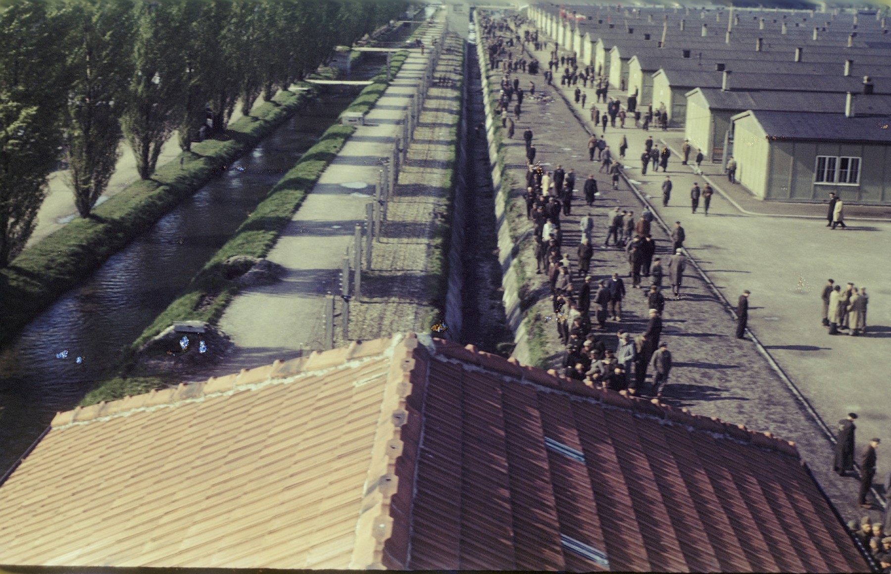 View from above of former prisoners walking along the main street of the newly liberated Dachau concentration camp parallel to the moat and the barbed wire fence.