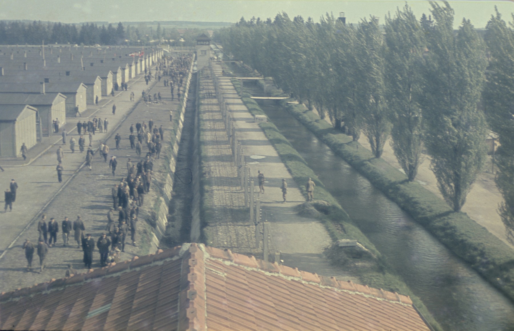 View from above of former prisoners walking along the main street of the newly liberated Dachau concentration camp parallel to the moats and barbed wire fence.