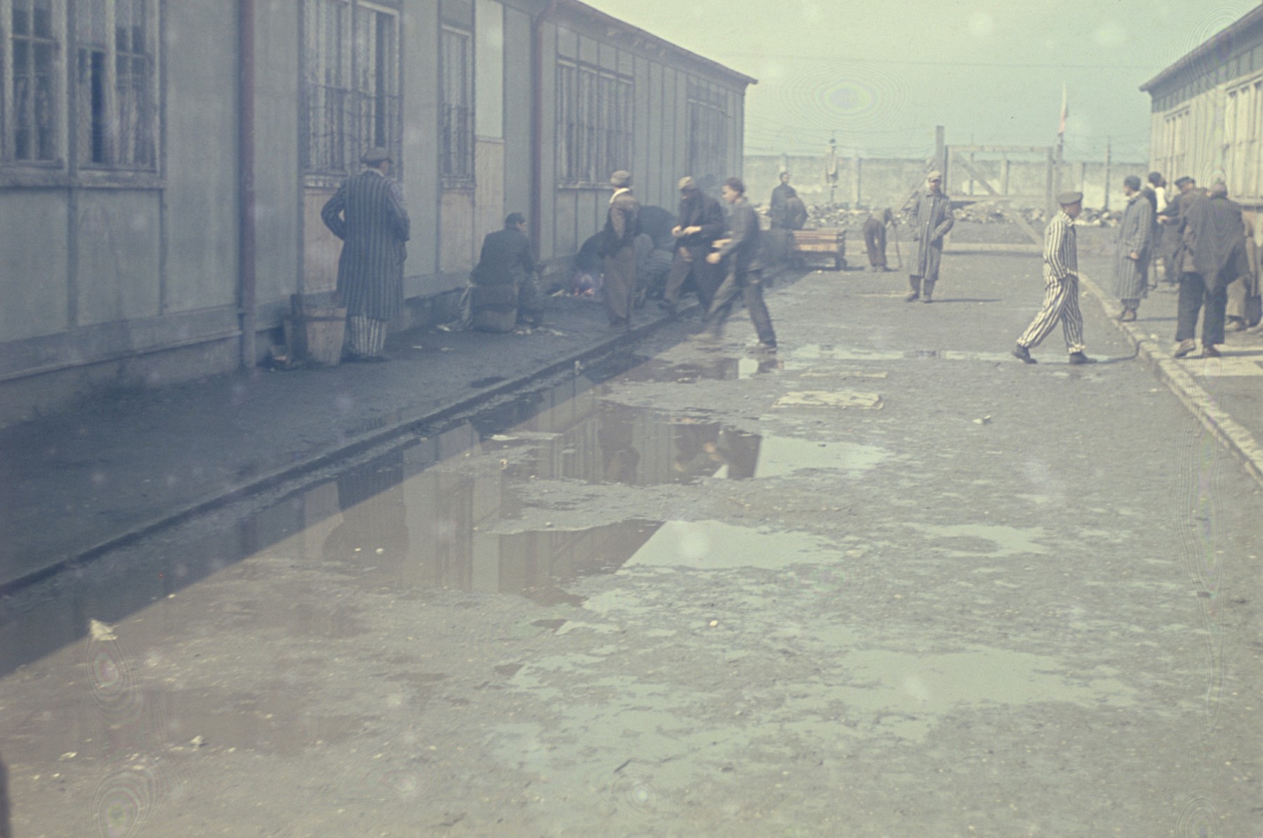 Former prisoners walk between two rows of barracks in the newly liberated Dachau concentration camp.