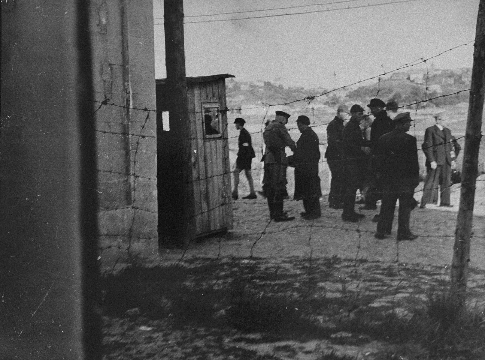 A group of Jews return to the ghetto after forced labor on the outside. German and Lithuanian guards search them as they enter. Jewish police stand among them.